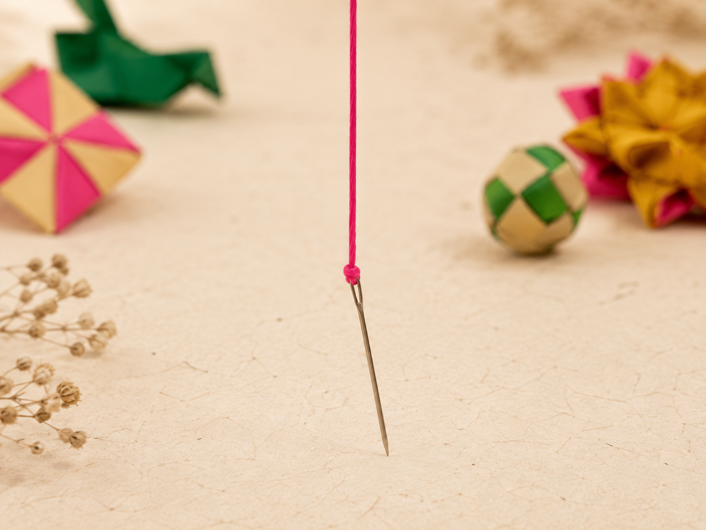 The needle tied to the free end of the pink thread, with several handmade ornaments in the background