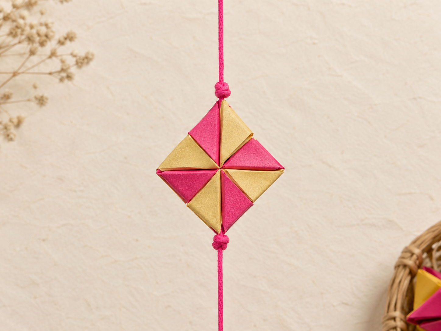 A close-up of a knot, then a geometric paper ornament, then another knot along the pink thread